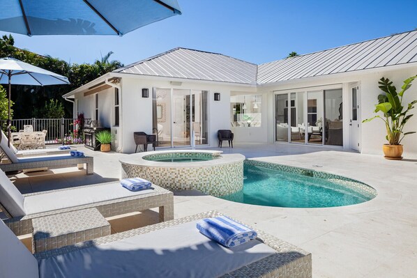A modern outdoor pool area with lounge chairs, a hot tub, and a covered patio.