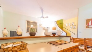 Une cuisine avec une table en bois, des chaises, un ventilateur de plafond, un cactus et des tableaux encadrés accrochés au mur.