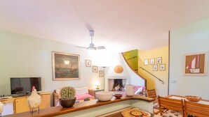 Un salon avec un téléviseur, un cactus, une cheminée et un coin repas comprenant une table et des chaises.