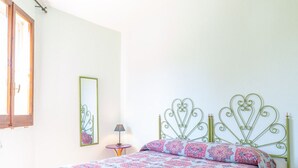 Une chambre à coucher avec un lit, une table de chevet, une lampe, une fenêtre et un miroir.