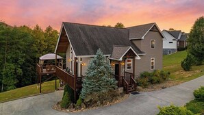 A two-story house with a covered porch and a small deck, surrounded by a well-maintained lawn and trees. - Relaxing Hideaway, Sleeps 11・Theater・Games・Hot Tub (Sevierville)