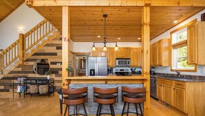 A kitchen with wooden cabinets, a central island with stools, a stainless steel refrigerator, and a microwave. - Relaxing Hideaway, Sleeps 11・Theater・Games・Hot Tub (Sevierville)