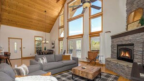 A spacious living room with a high ceiling, large windows, a stone fireplace, and a cozy seating area. - Relaxing Hideaway, Sleeps 11・Theater・Games・Hot Tub (Sevierville)