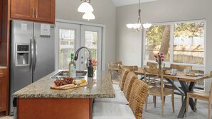 A kitchen with a granite countertop, stainless steel appliances, wooden cabinets, and a dining area with a table and chairs. - Pelican Retreat by Avantstay 5 Mins TO Beach Pet Friendly w/ Pool & Bbq! (Destin)