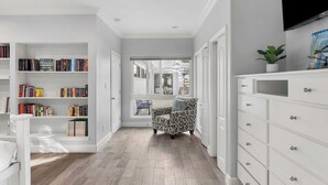 A hallway with a bookshelf, a patterned armchair, and a white dresser. - Pelican Retreat by Avantstay 5 Mins TO Beach Pet Friendly w/ Pool & Bbq! (Destin)