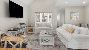 A spacious living room with a ceiling fan, a flat-screen TV, white sofas, and a coffee table. - Pelican Retreat by Avantstay 5 Mins TO Beach Pet Friendly w/ Pool & Bbq! (Destin)