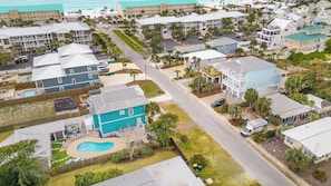 An aerial view of a coastal residential area with multiple two-story buildings, a swimming pool, and a road.