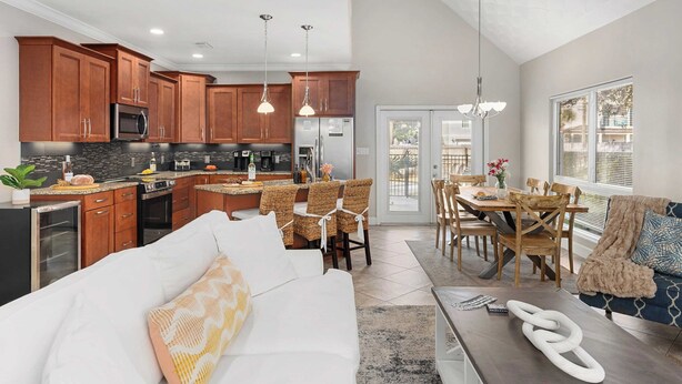 A modern kitchen with wooden cabinets, stainless steel appliances, and a dining area with wicker chairs and a wooden table. - Pelican Retreat by Avantstay 5 Mins TO Beach Pet Friendly w/ Pool & Bbq! (Destin)