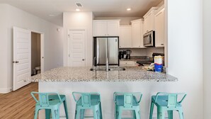 A kitchen with white cabinets, a stainless steel refrigerator, a granite countertop, and three turquoise bar stools. - Santa Rosa Hideaway by Avantstay Pet Friendly 6 Mins to Beach! (Santa Rosa Beach)