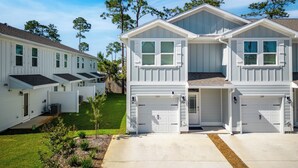 A row of two-story townhouses with attached garages, a well-maintained lawn, and mature trees in the background. - Santa Rosa Hideaway by Avantstay Pet Friendly 6 Mins to Beach! (Santa Rosa Beach)