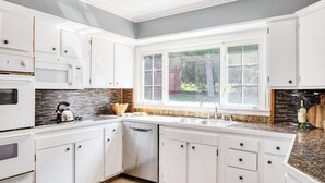 Una cocina moderna con armarios blancos, encimera de granito, horno empotrado y ventana con vistas a un jardín.