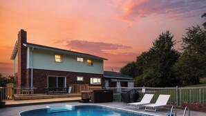 Una casa de dos pisos con piscina, terraza y mobiliario exterior.