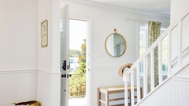Una habitación con un banco de madera, una puerta blanca, un espejo y una escalera.