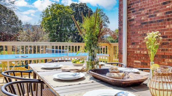 An outdoor dining area with a wooden table set for two, surrounded by chairs.