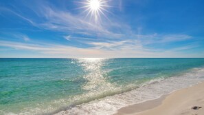 Une plage à l’eau claire, avec un rivage sablonneux et un soleil éclatant.