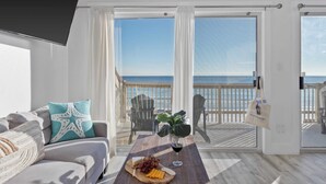 A balcony with a view of the sea, a table with food and drink, and a sofa with a starfish pillow. - Destiny on the Sand by Avantstay Direct Beach Access! Bbq on Large Ocean Facing Patio (Destin)