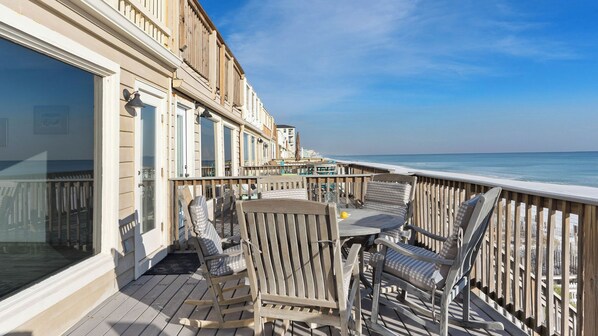 A wooden deck with outdoor seating, overlooking a beach.
