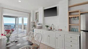A modern kitchen with a large window, white cabinetry, and a flat-screen TV. - Destiny on the Sand by Avantstay Direct Beach Access! Bbq on Large Ocean Facing Patio (Destin)