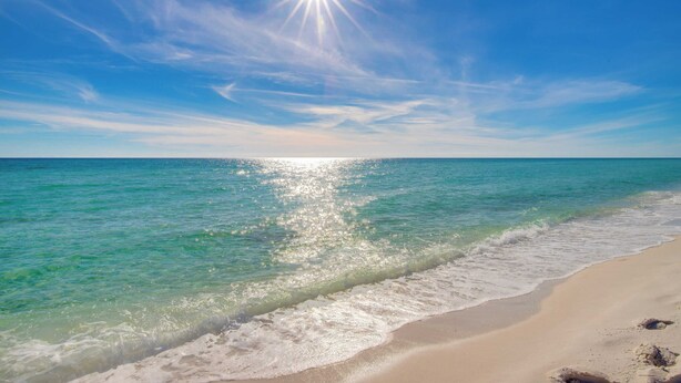 A beach with clear turquoise water, a sandy shore, and a bright sun in the sky. - Destiny on the Sand by Avantstay Direct Beach Access! Bbq on Large Ocean Facing Patio (Destin)