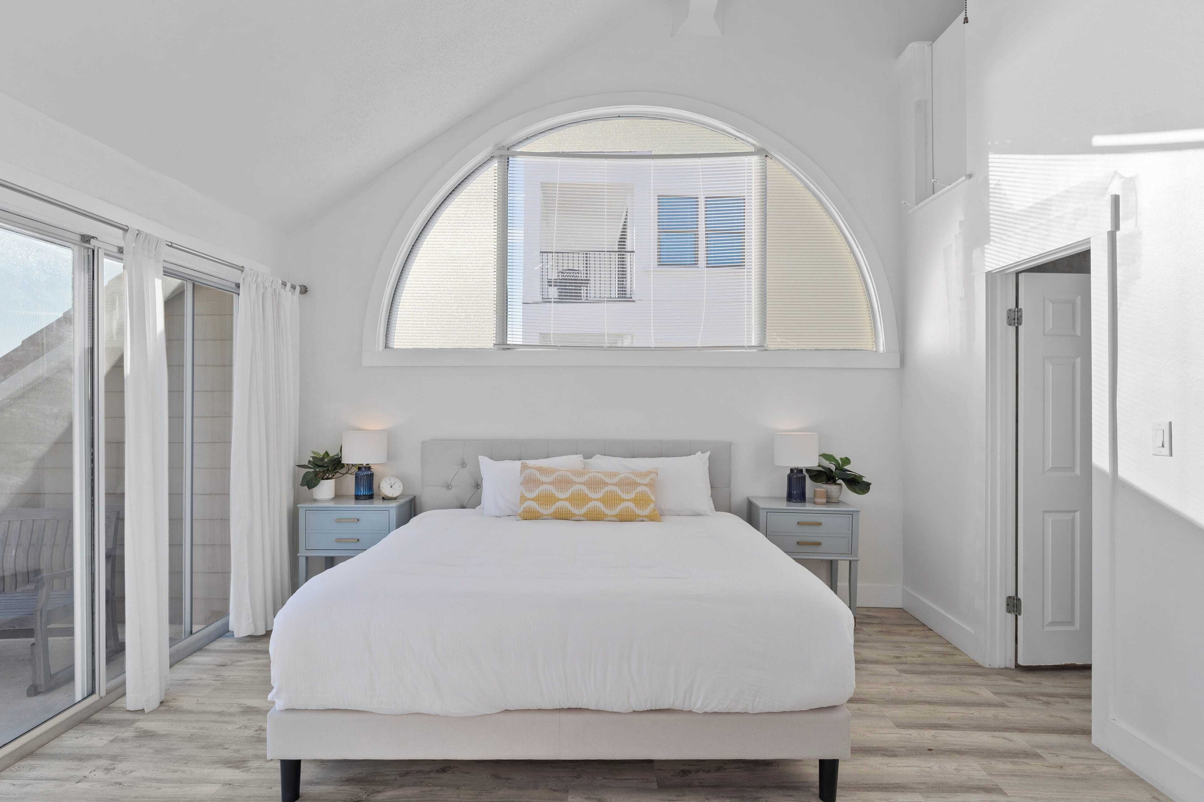 A bedroom with a large bed, a skylight, a sliding glass door, and a nightstand with a lamp.