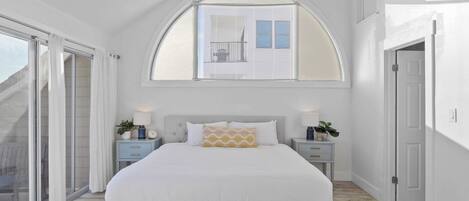 A bedroom with a large bed, a skylight, a sliding glass door, and a nightstand with a lamp.