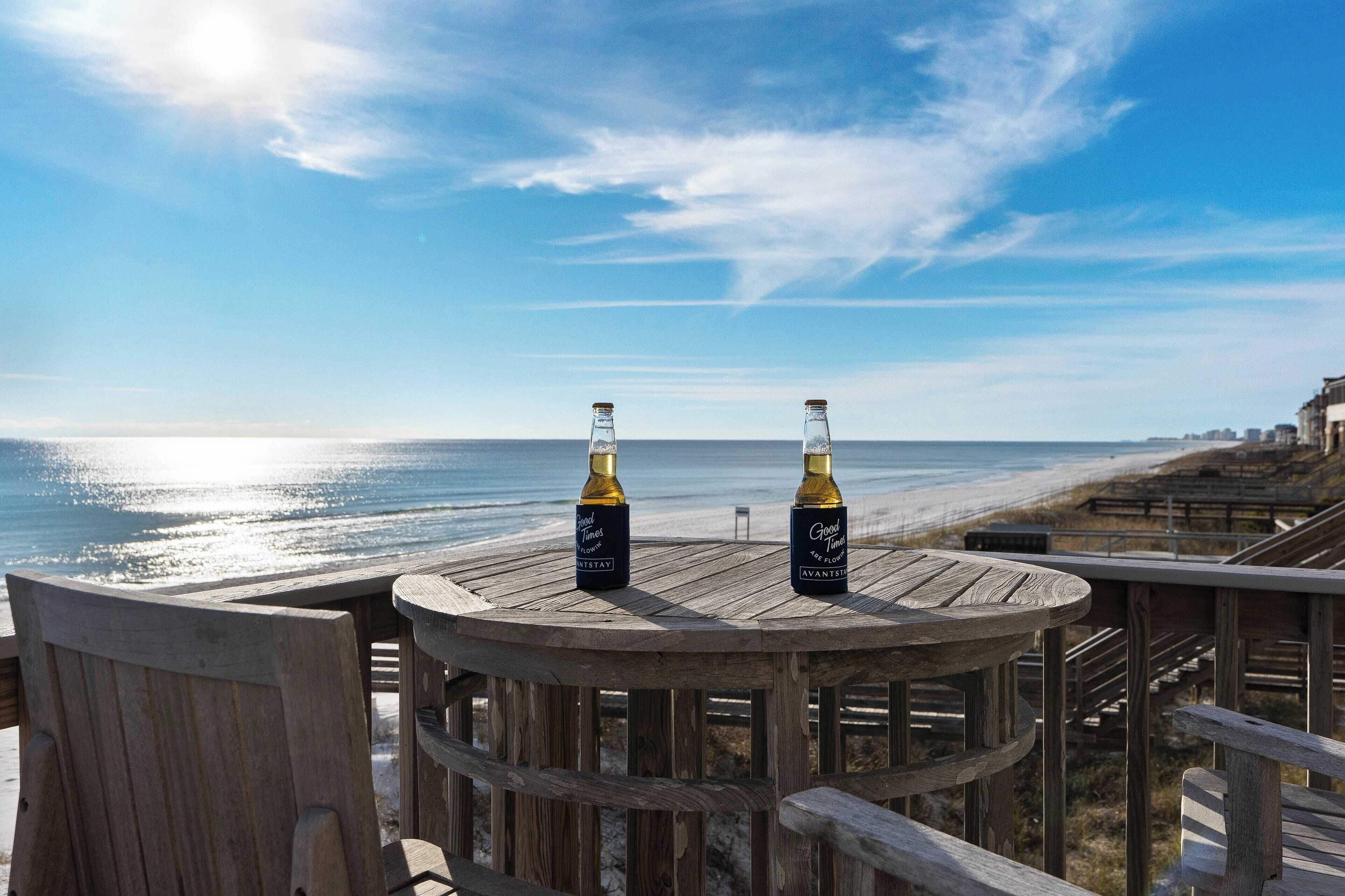 A wooden deck with two bottles of wine, overlooking a beach.