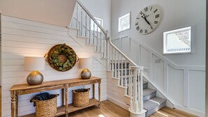 Eine Treppe mit weißen Geländern und Holzboden, eine Wanduhr und ein Konsolentisch mit Körben und Dekoration.