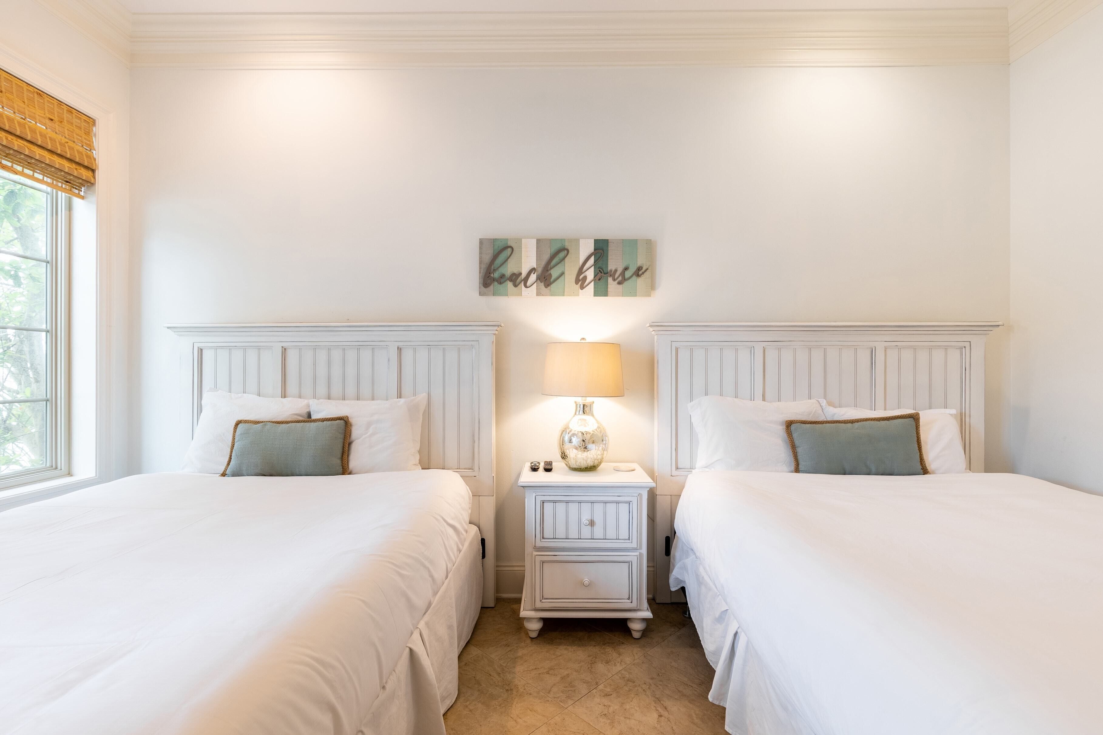 A bedroom with two beds, a nightstand with a lamp, and a wall sign.