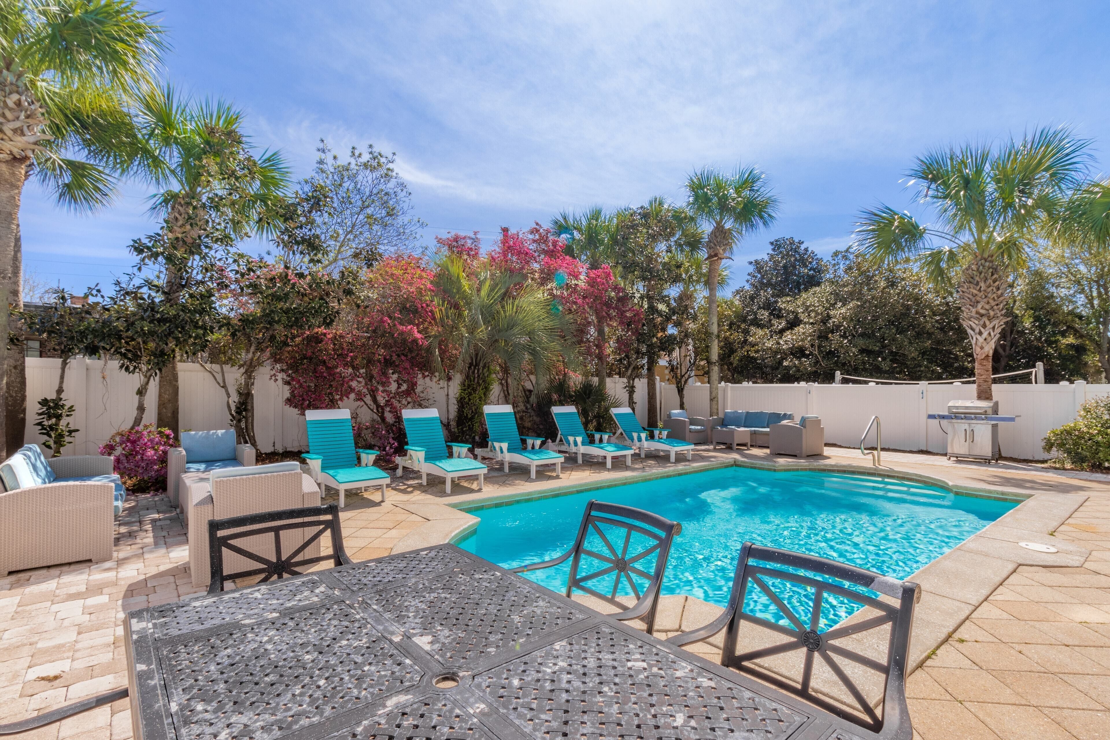 A backyard with a swimming pool, lounge chairs, and various plants.
