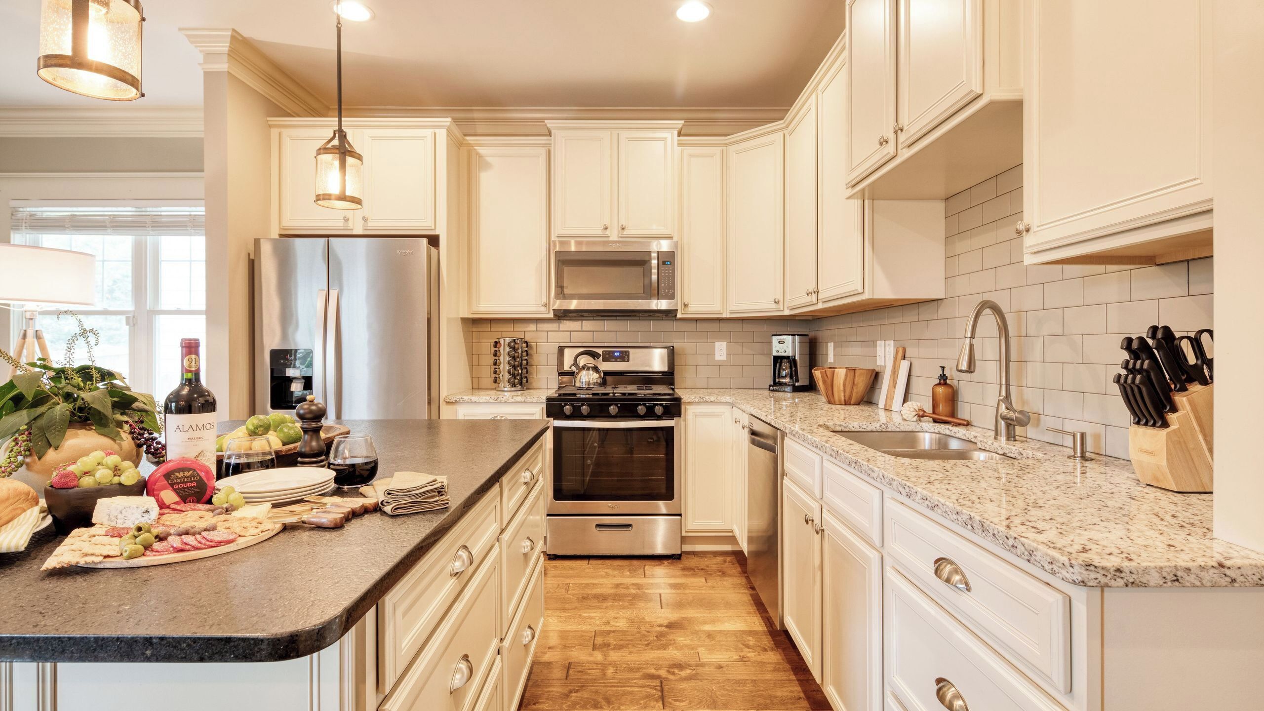Una cocina moderna con armarios blancos, electrodomésticos de acero inoxidable, encimera de granito y piso de madera.