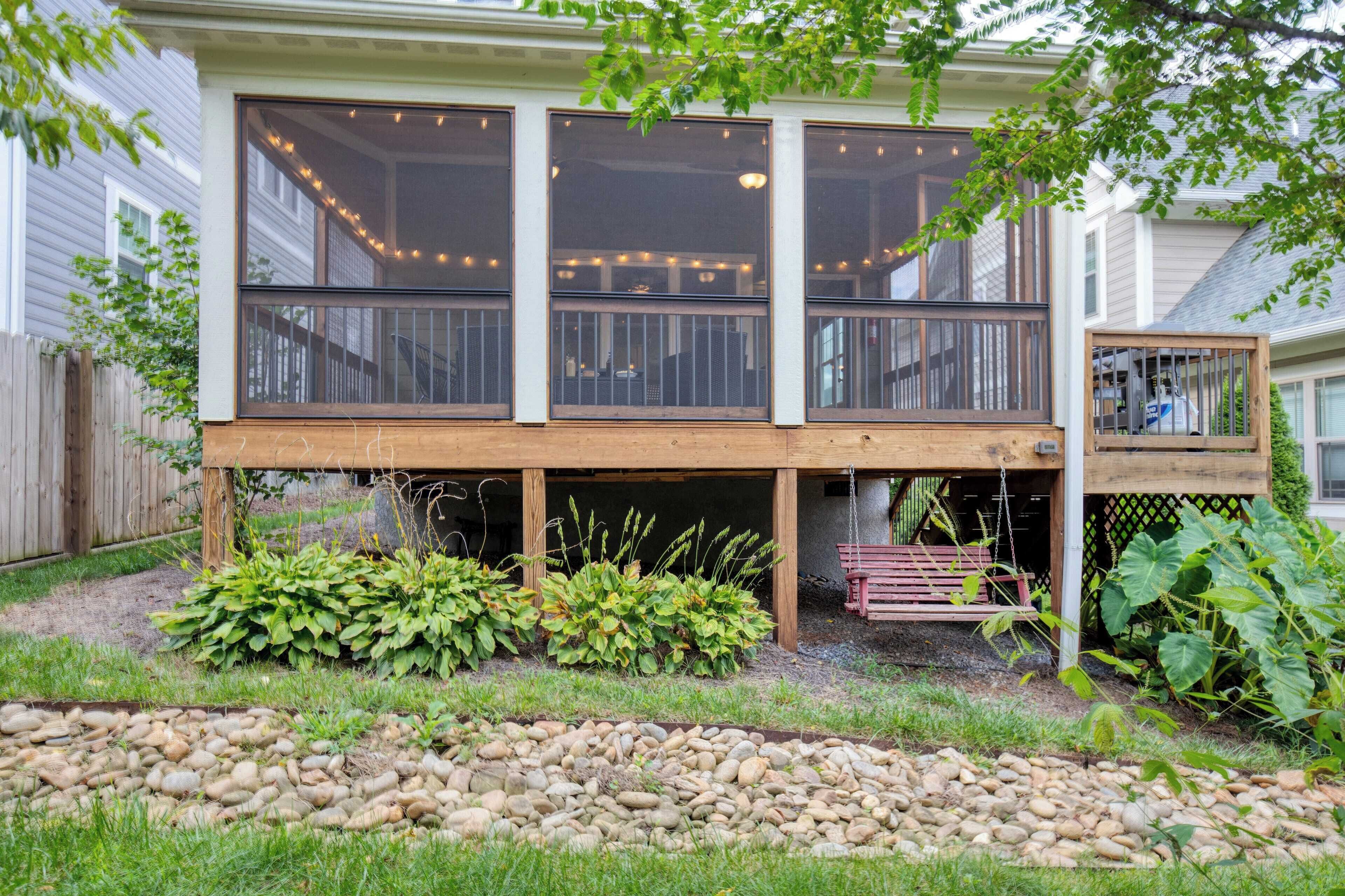 A two-story deck with a wooden railing, surrounded by a garden with various plants and a pebble pathway.