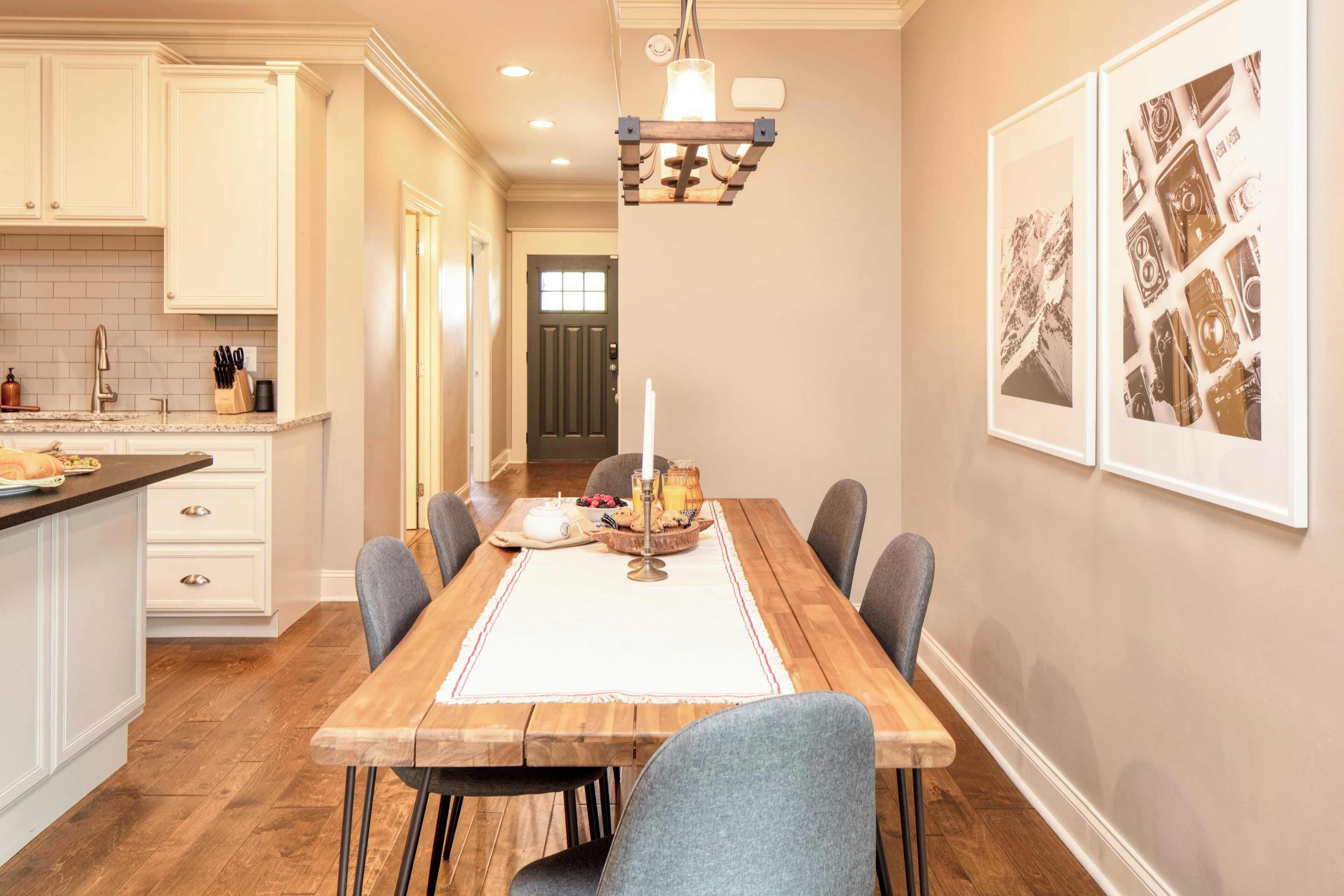 A dining area with a wooden table, chairs, a chandelier, and framed pictures on the wall.
