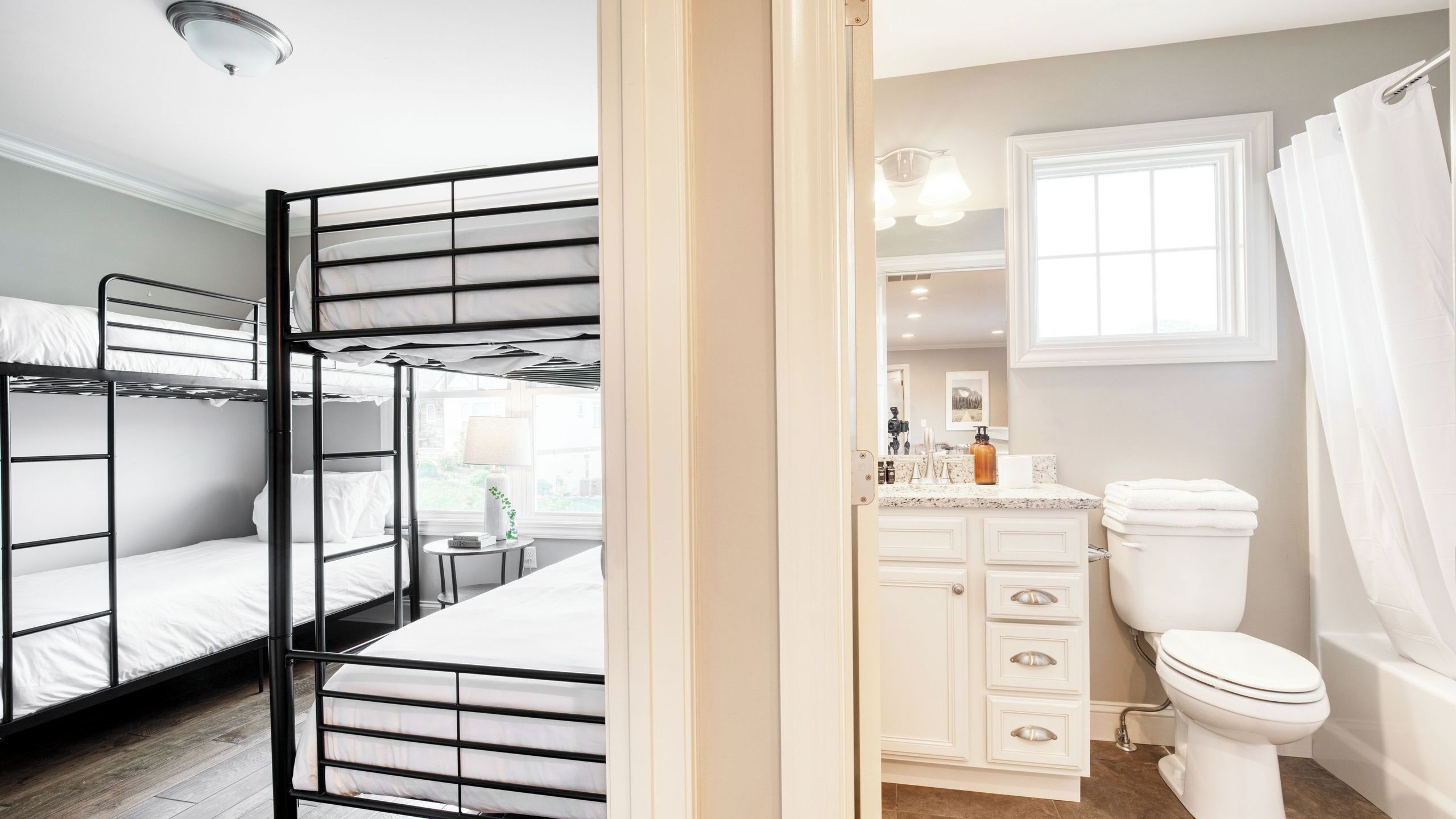 A room with bunk beds, a bathroom with a toilet and sink, and a window with curtains.