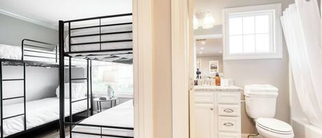 A room with bunk beds, a bathroom with a toilet and sink, and a window with curtains.
