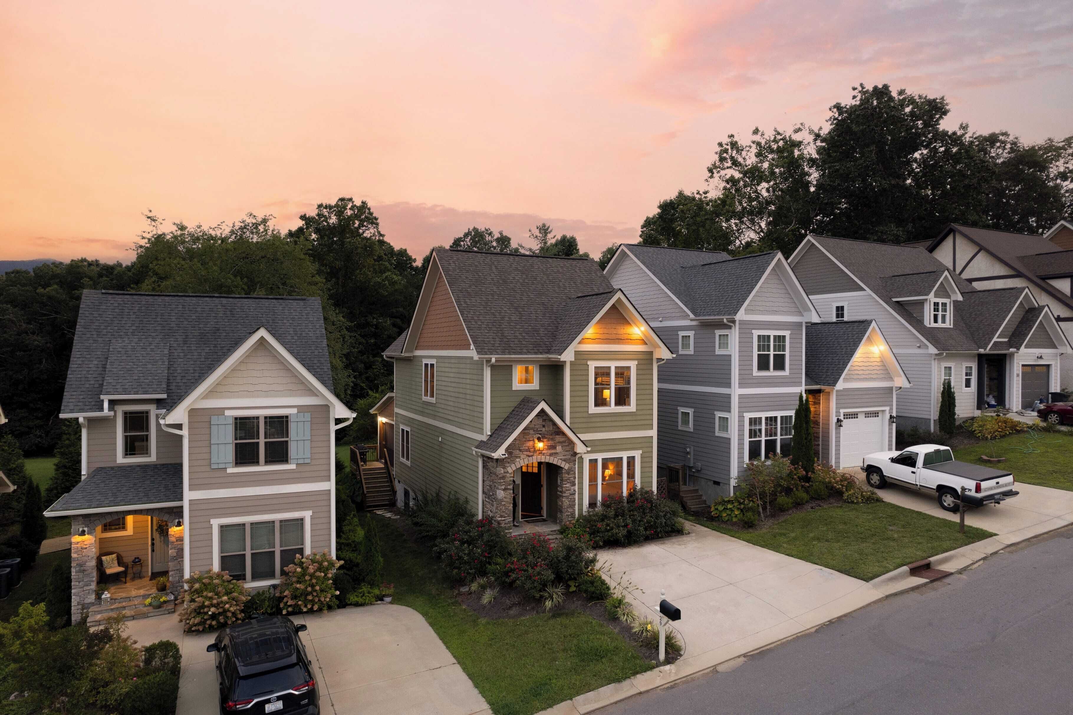 A row of two-story houses with attached garages, a driveway, and a parked car.