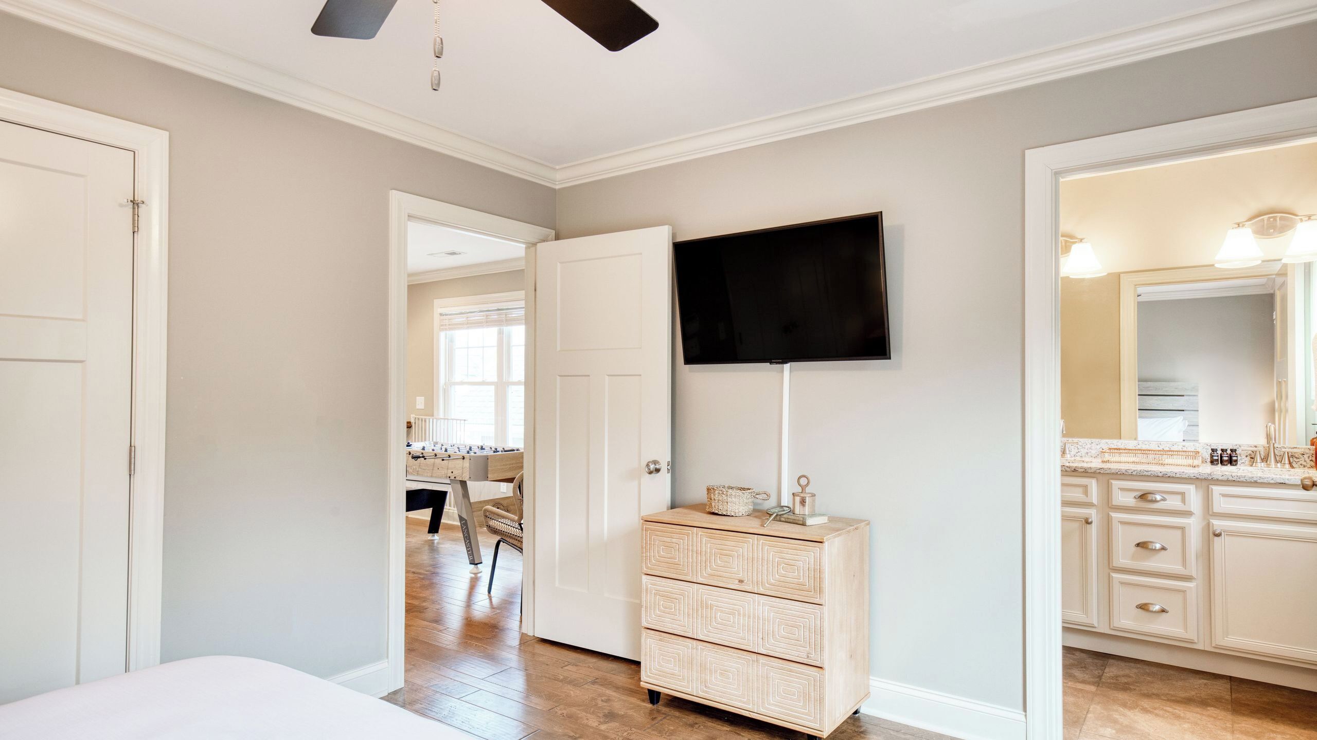A bedroom with a bed, a dresser, a television, and a bathroom with a mirror and sink.