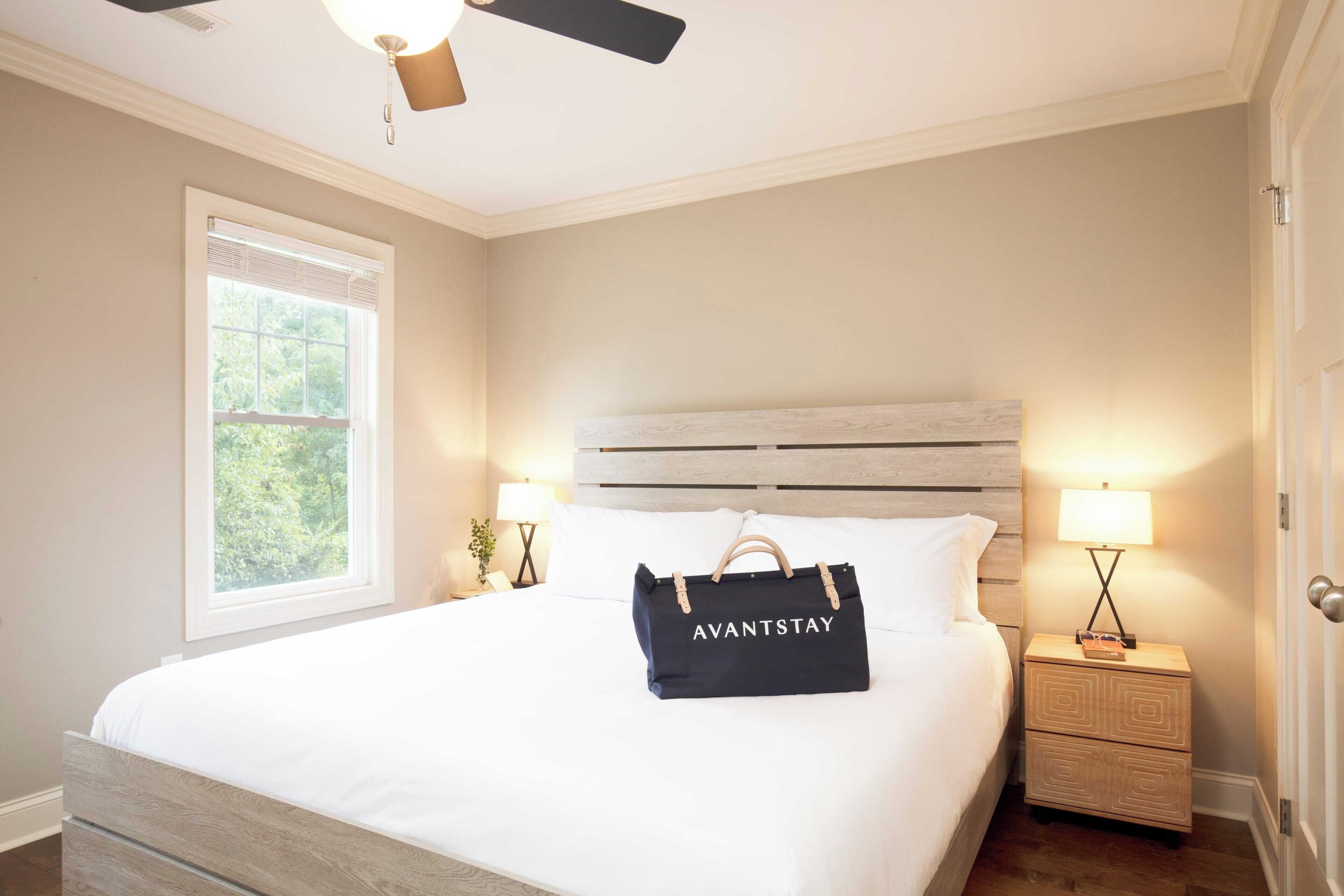 A bedroom with a bed, a nightstand, a lamp, a ceiling fan, and a window.