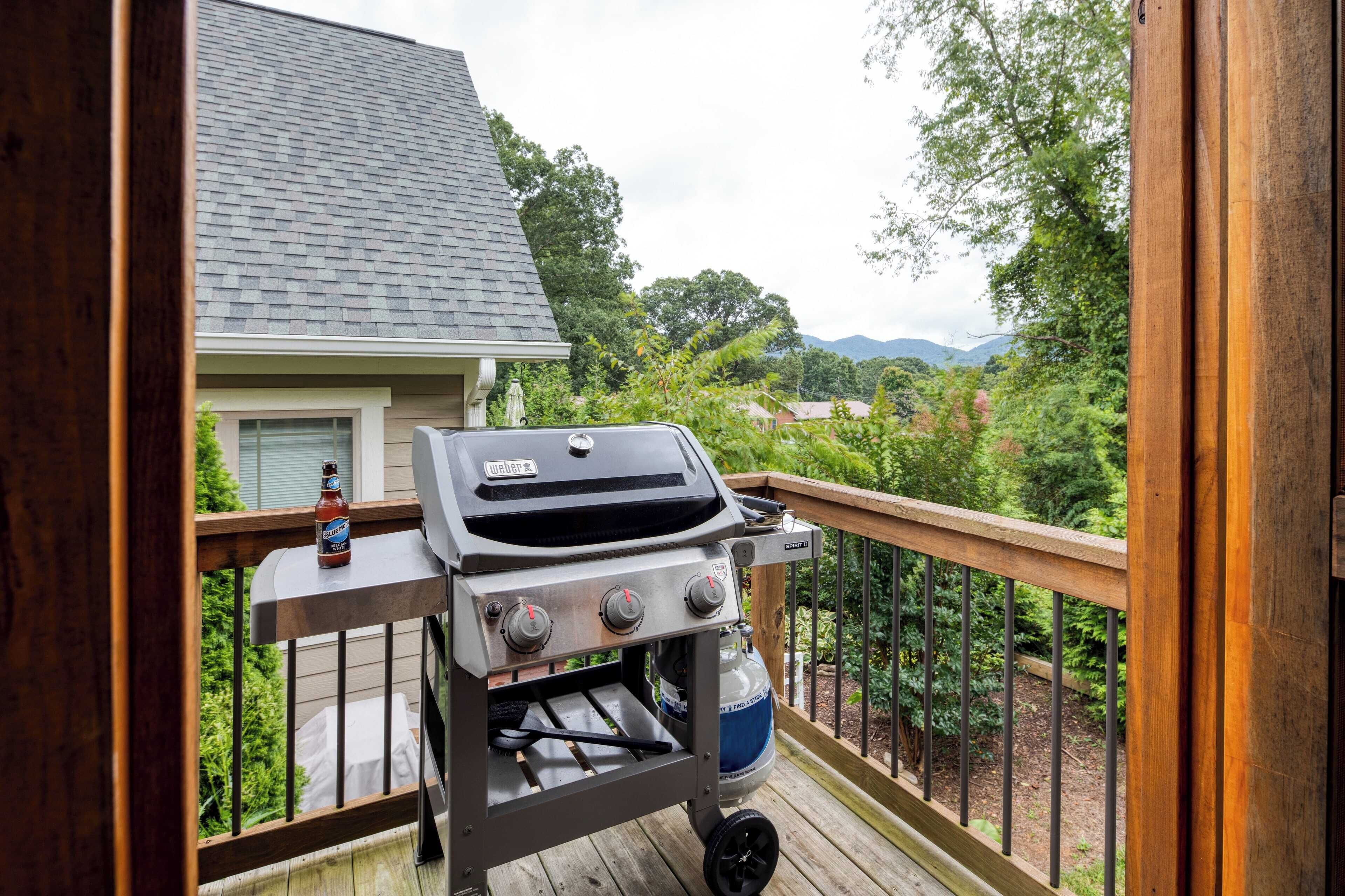 A barbecue grill on a wooden deck with a view of a house and greenery in the background.