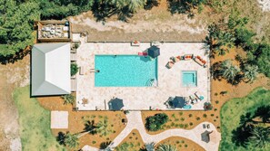 En vy över en fastighet, tagen från luften, som visar en pool, utomhusmöbler och ett takförsett område med en grill.