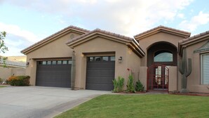 A two-story house with a garage, a front entrance with a red gate, and a well-maintained lawn. - RANCHO MIRAGE - VICTORIA FALLS ENTERTAINING 4 BD - HUGE POOL & SPA & GRASS YARD! (Rancho Mirage)