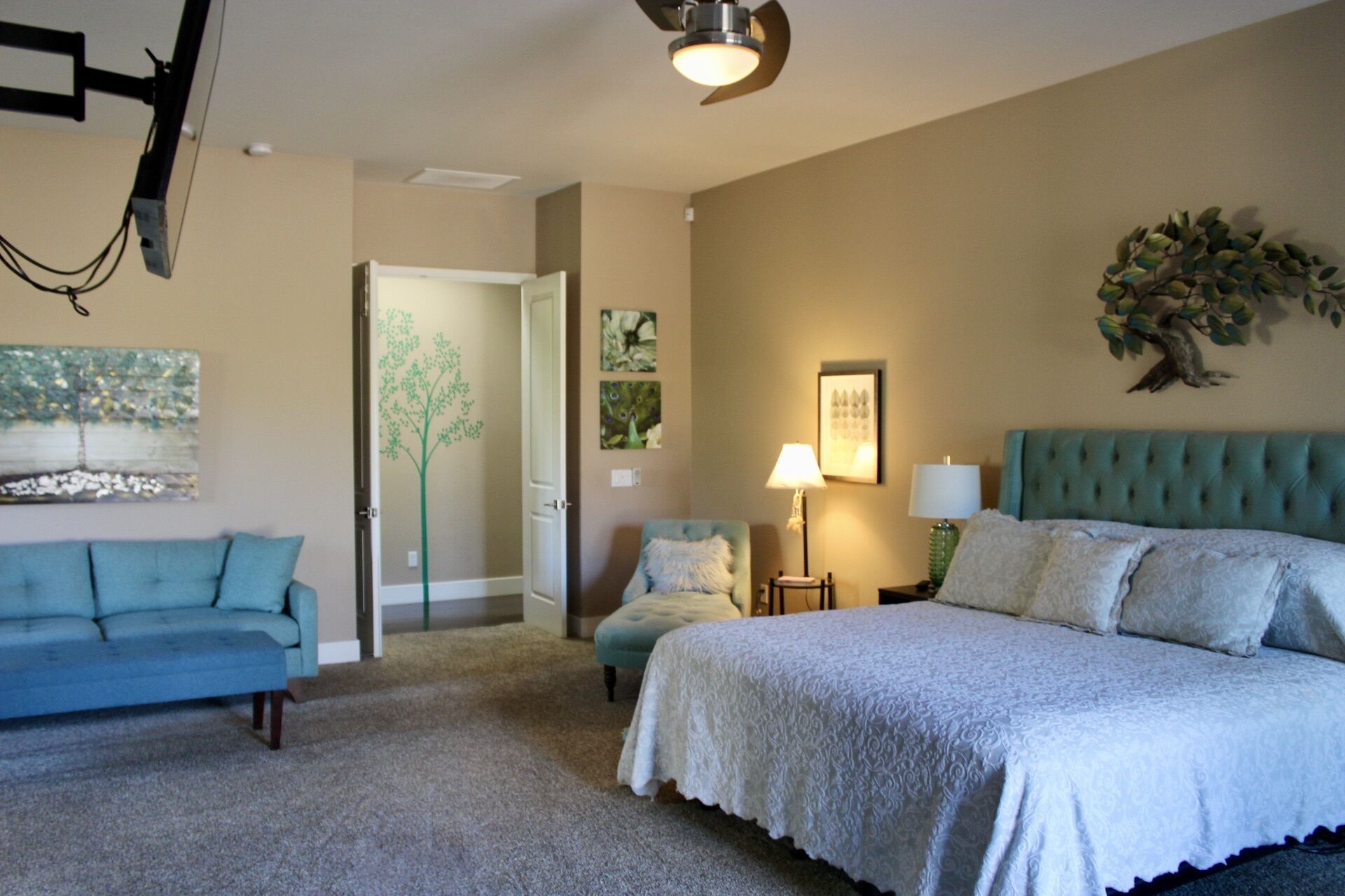 A bedroom with a bed, a blue sofa, a chair, a lamp, and wall art.