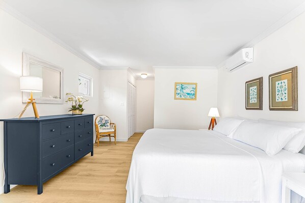 A bedroom with a large bed, a dark blue dresser, a chair, and a small table with a lamp.