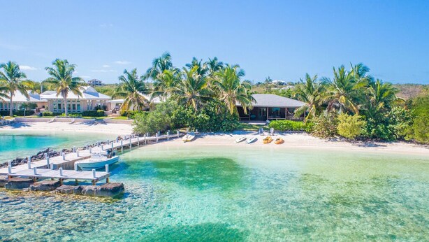 A coastal resort with clear turquoise waters, a dock with boats, and palm trees.