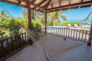 Eine Hängematte auf einem gefliesten Balkon mit Pool und Palmen im Hintergrund.