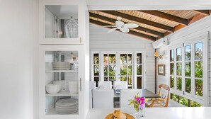 A bright kitchen with white cabinetry, a dining area with a table and chairs, and large windows with a view of greenery.