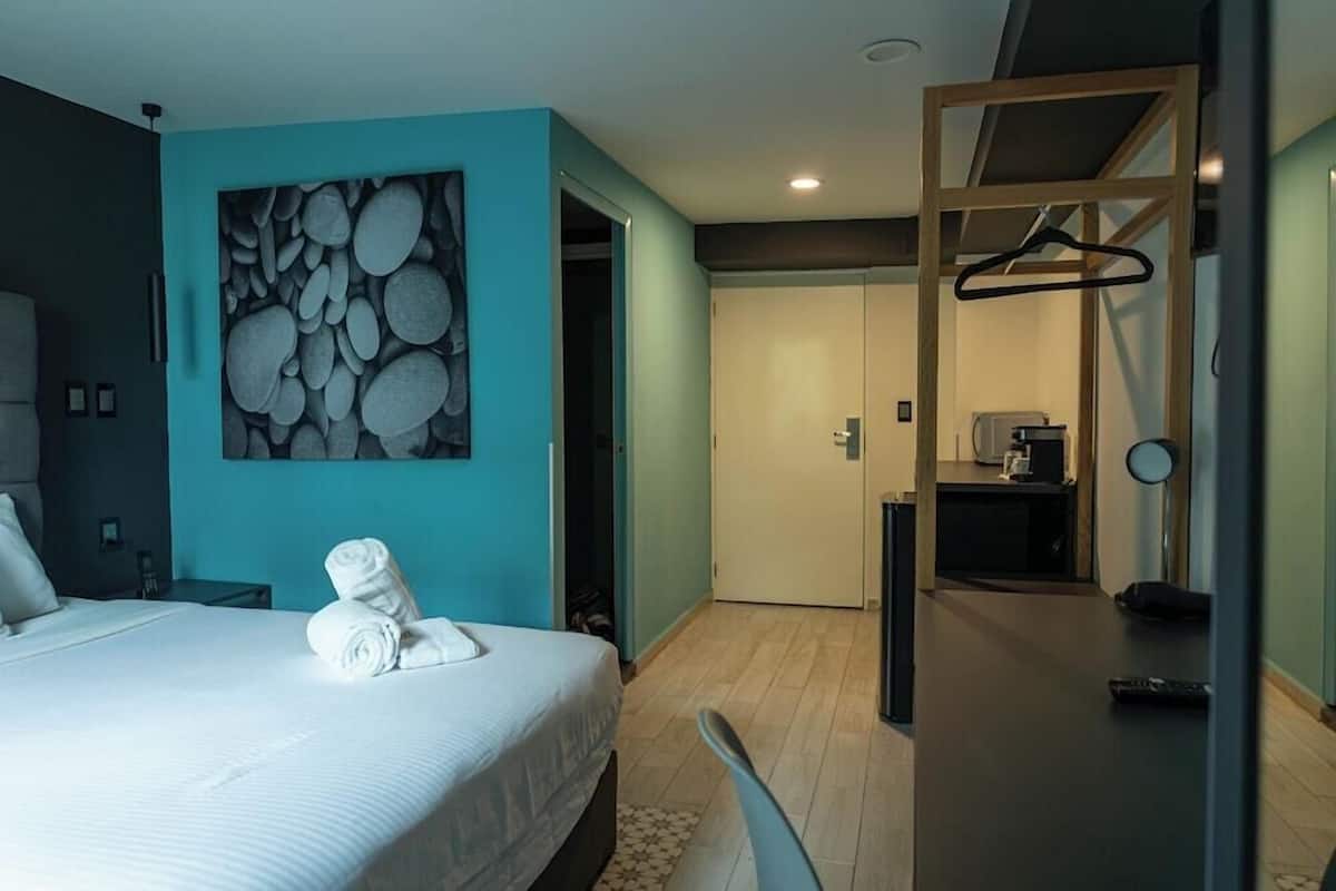 Une chambre d’hôtel moderne équipée d’un lit, d’un tableau, d’un bureau et d’une kitchenette.