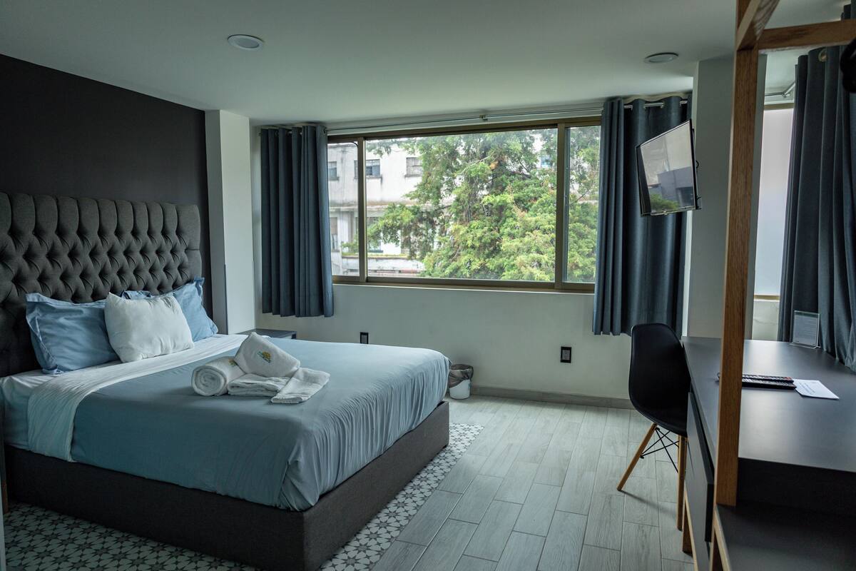 Une chambre d’hôtel moderne avec un grand lit, un bureau et une fenêtre avec des rideaux.