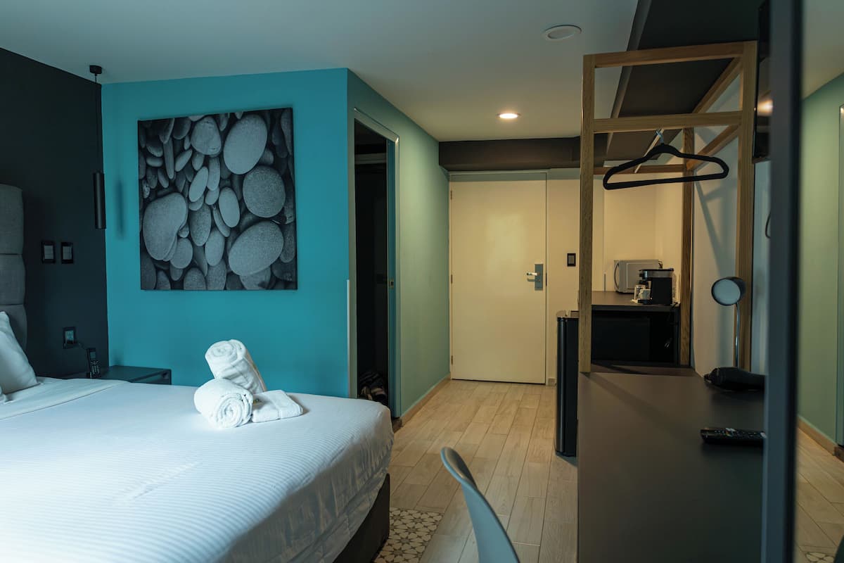 Une chambre d’hôtel avec un lit, un tableau, un bureau et une kitchenette.