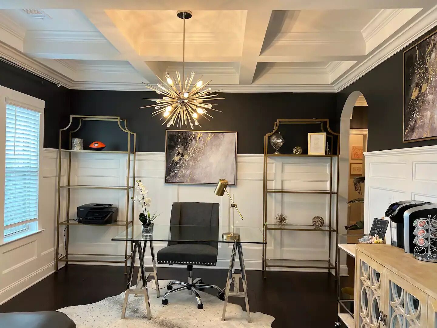 Een moderne kantoorruimte met een glazen bureau, een zwarte bureaustoel en een bijzondere plafondlamp.