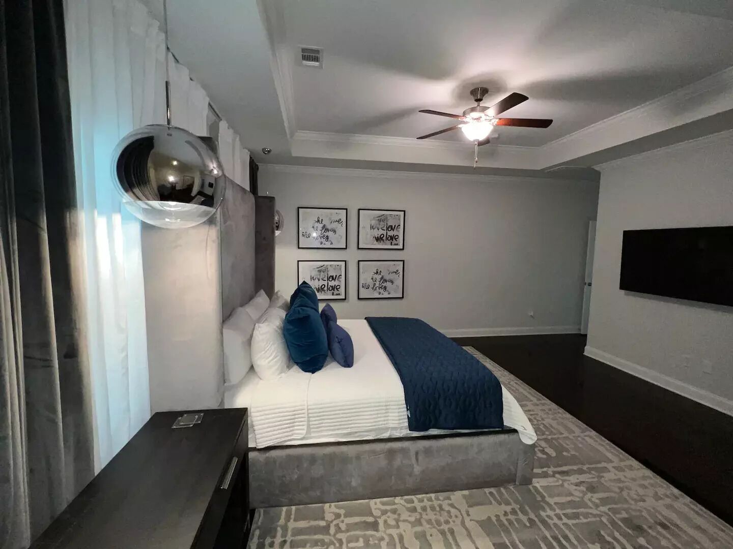 A modern bedroom with a bed, a ceiling fan, and framed wall art.